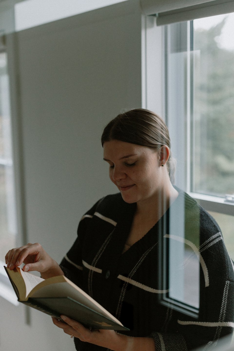 Woman in striped cardigan smiles while reading a book.